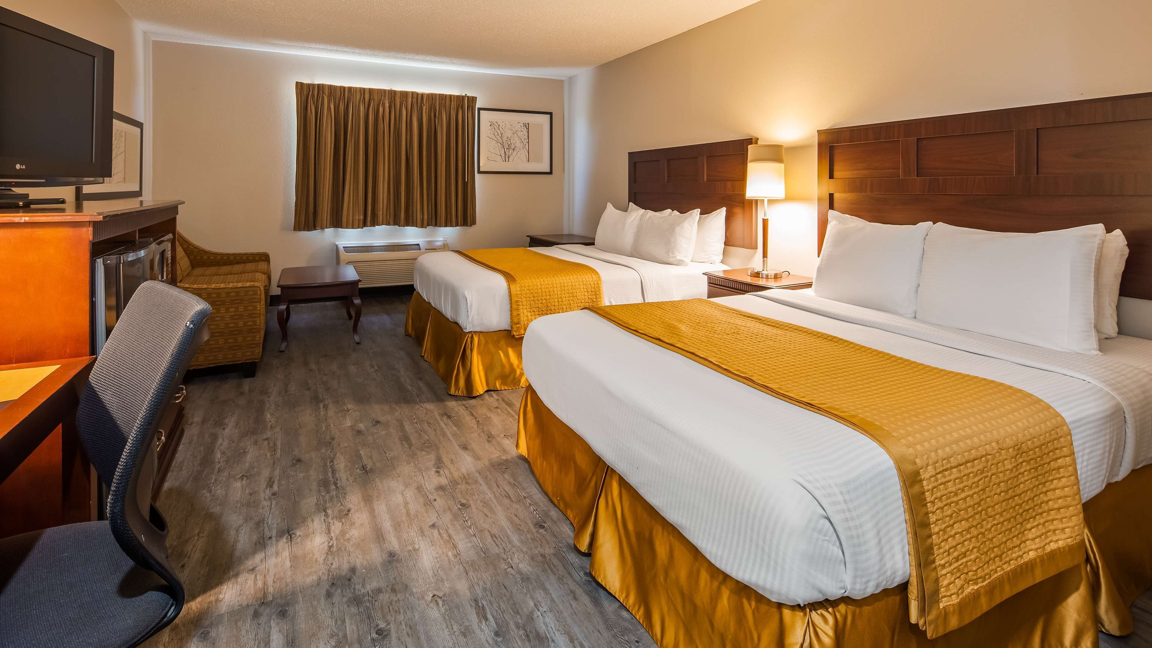 A hotel room with two beds, a desk, a chair, a TV, and a window with curtains.