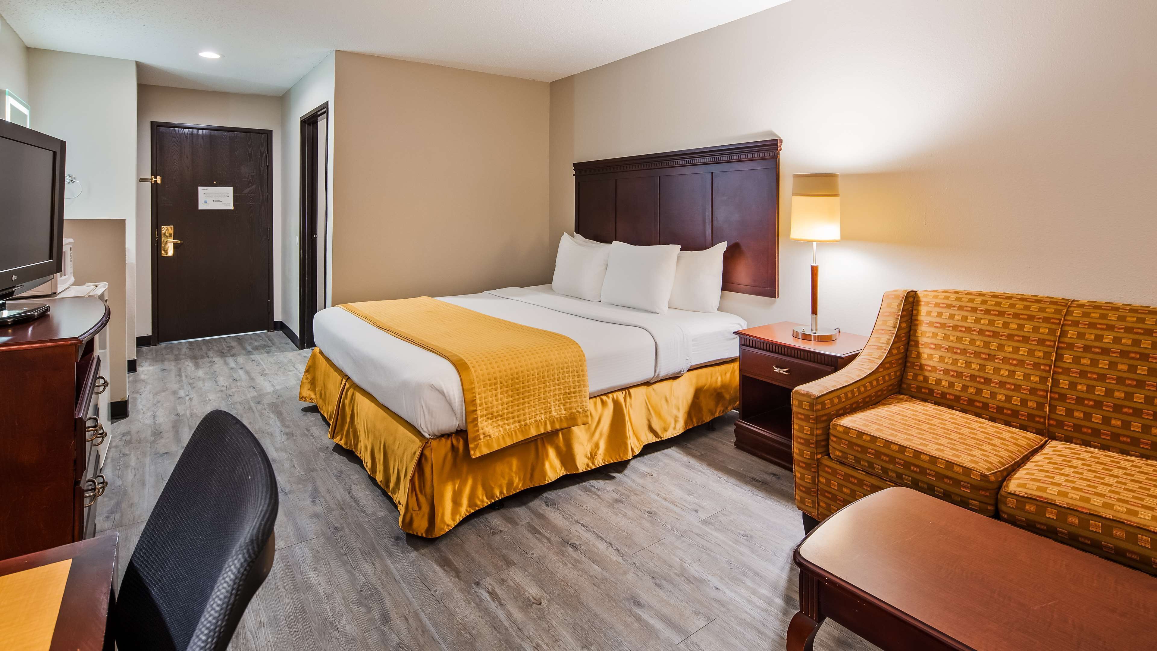 A hotel room with a bed, a desk, a chair, a TV, and a lamp.