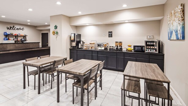 A modern kitchen with wooden tables and chairs, a coffee station, and a 'Welcome' sign. - SureStay Hotel by Best Western Orange (Orange)