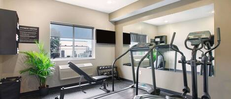 A fitness center with a treadmill, elliptical, and weight bench.