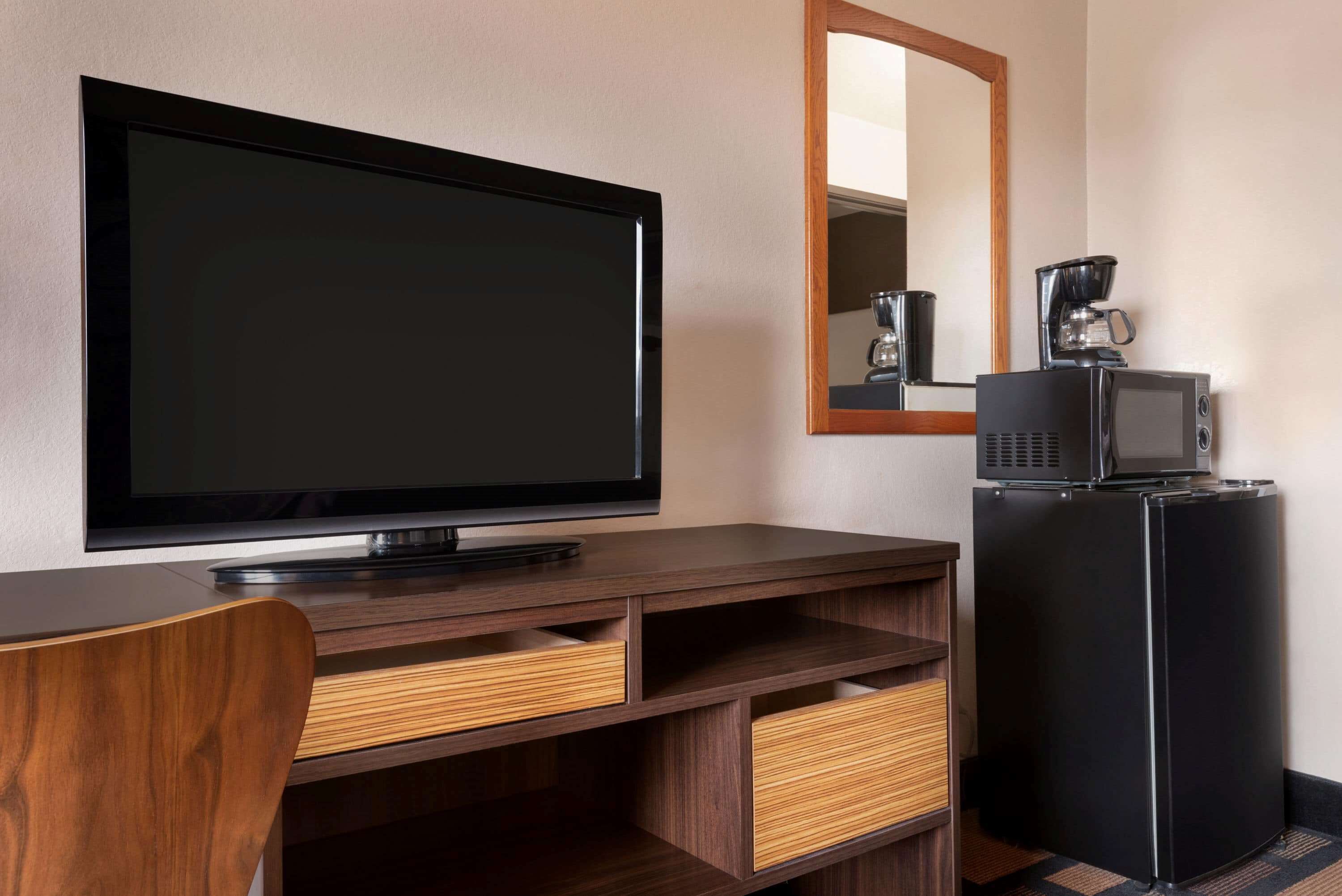 A hotel room with a flat-screen TV, a coffee maker, and a refrigerator.