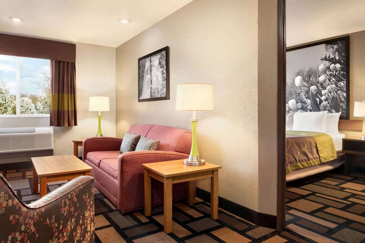 A hotel room with a sofa, a chair, a small table, two lamps, a bed, and a large framed picture on the wall.