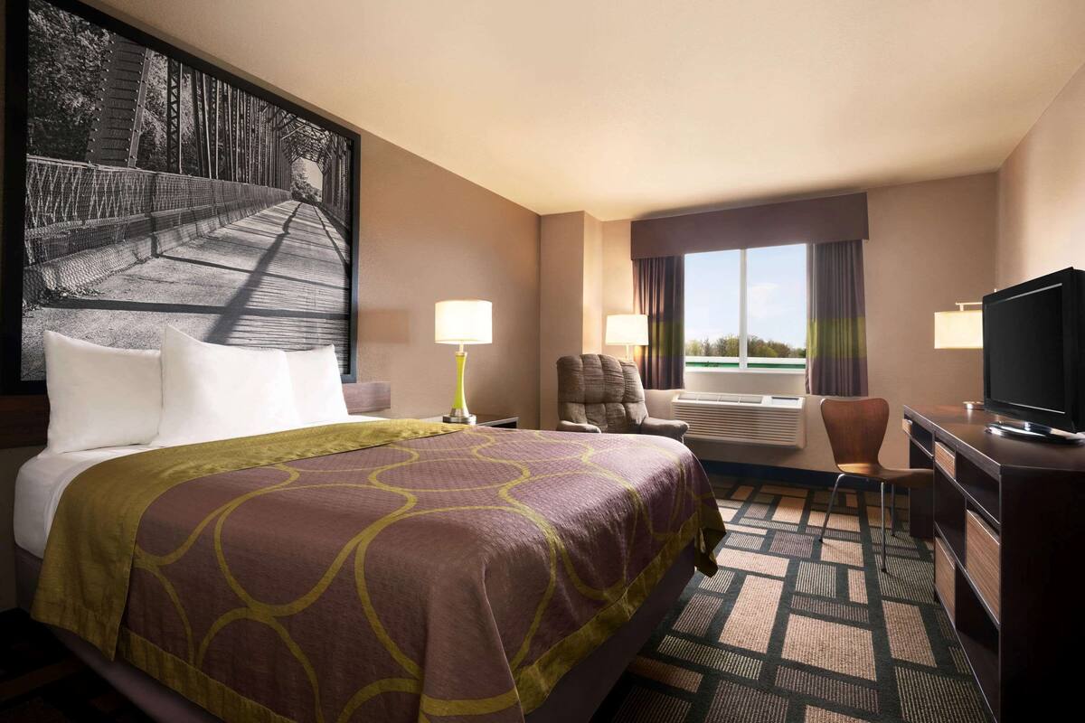 A hotel room with a large bed, two chairs, a desk, a television, and a window with curtains.