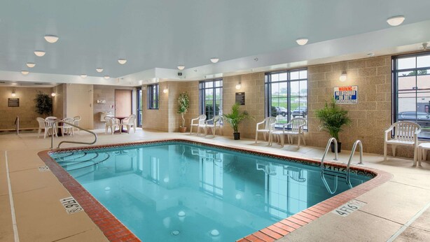 Una piscina interior con agua cristalina, rodeada de sillas blancas y plantas en macetas.