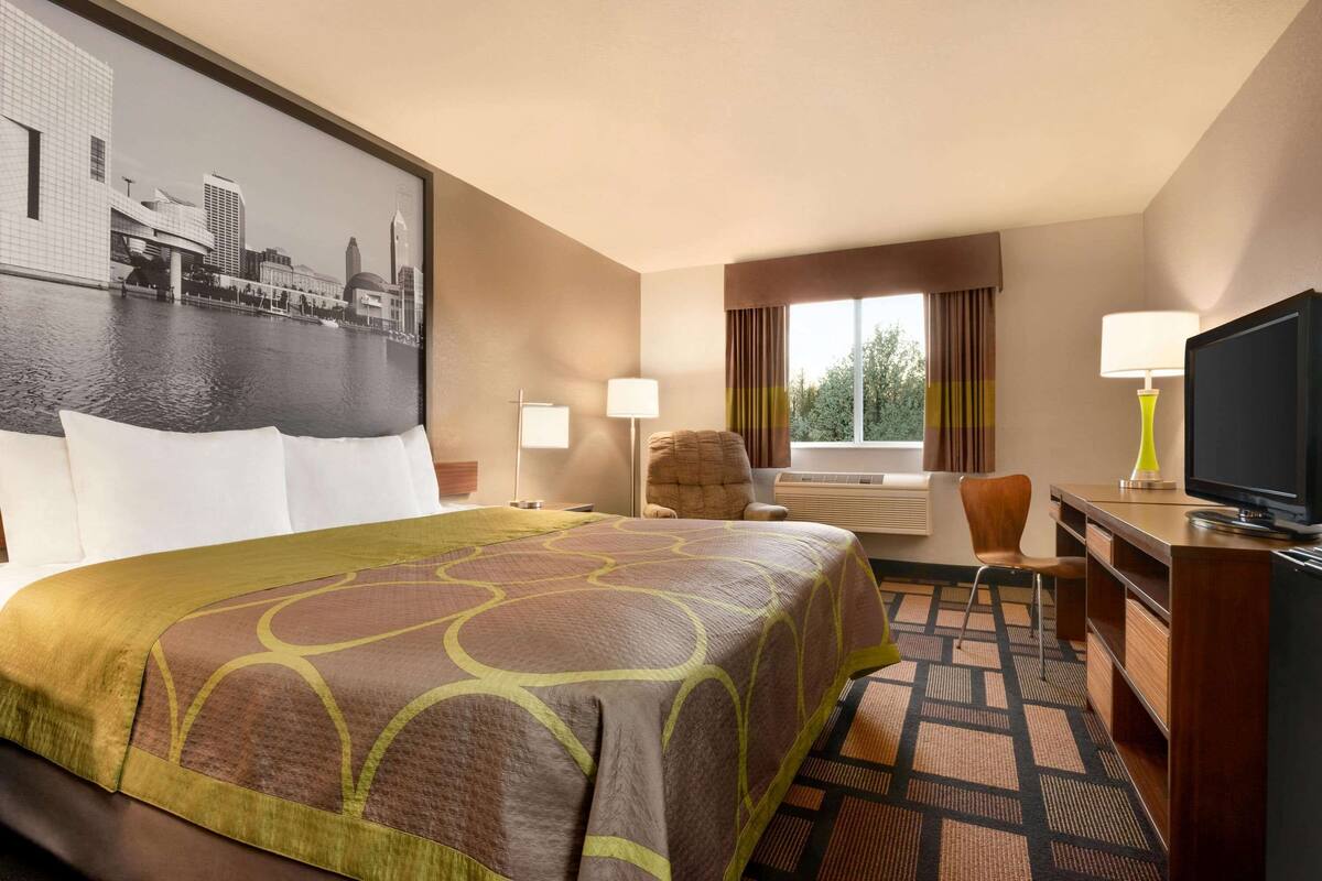 A hotel room with a large bed, a desk, a chair, a television, and a window with curtains.