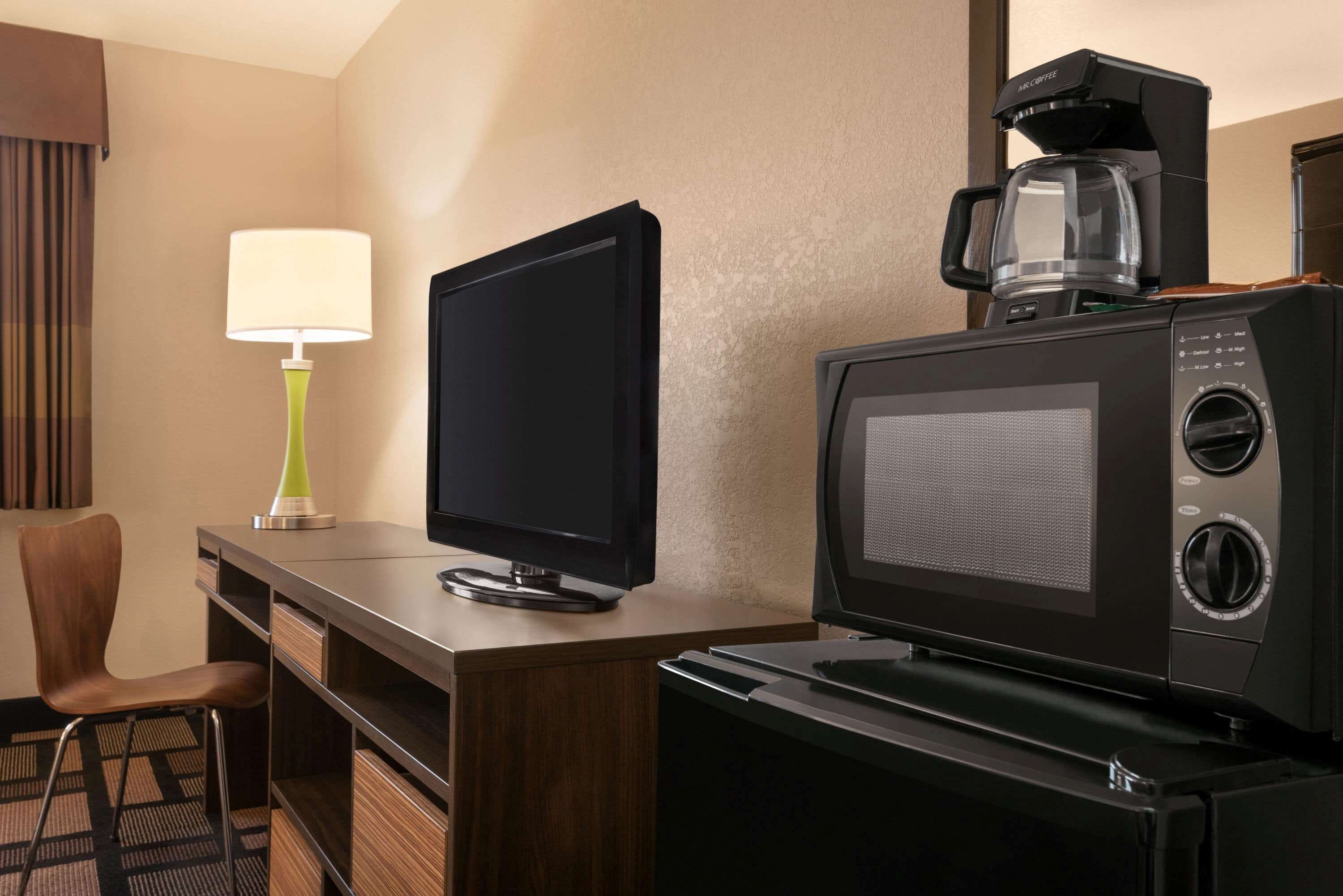 Una camera d'albergo con TV a schermo piatto, macchina del caffè, lampada e una sedia.