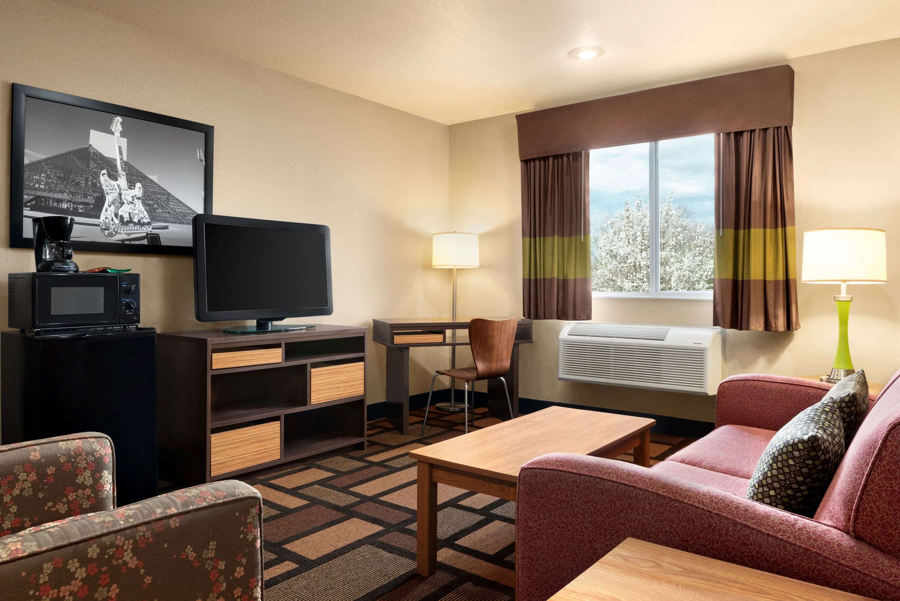 Une chambre d’hôtel équipée d’une télévision, d’un bureau, d’une chaise, d’un canapé et d’une fenêtre avec des rideaux.