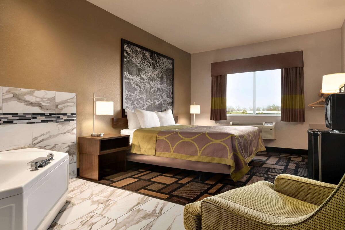 A hotel room with a bed, a sitting area, a bathtub, and a large window.