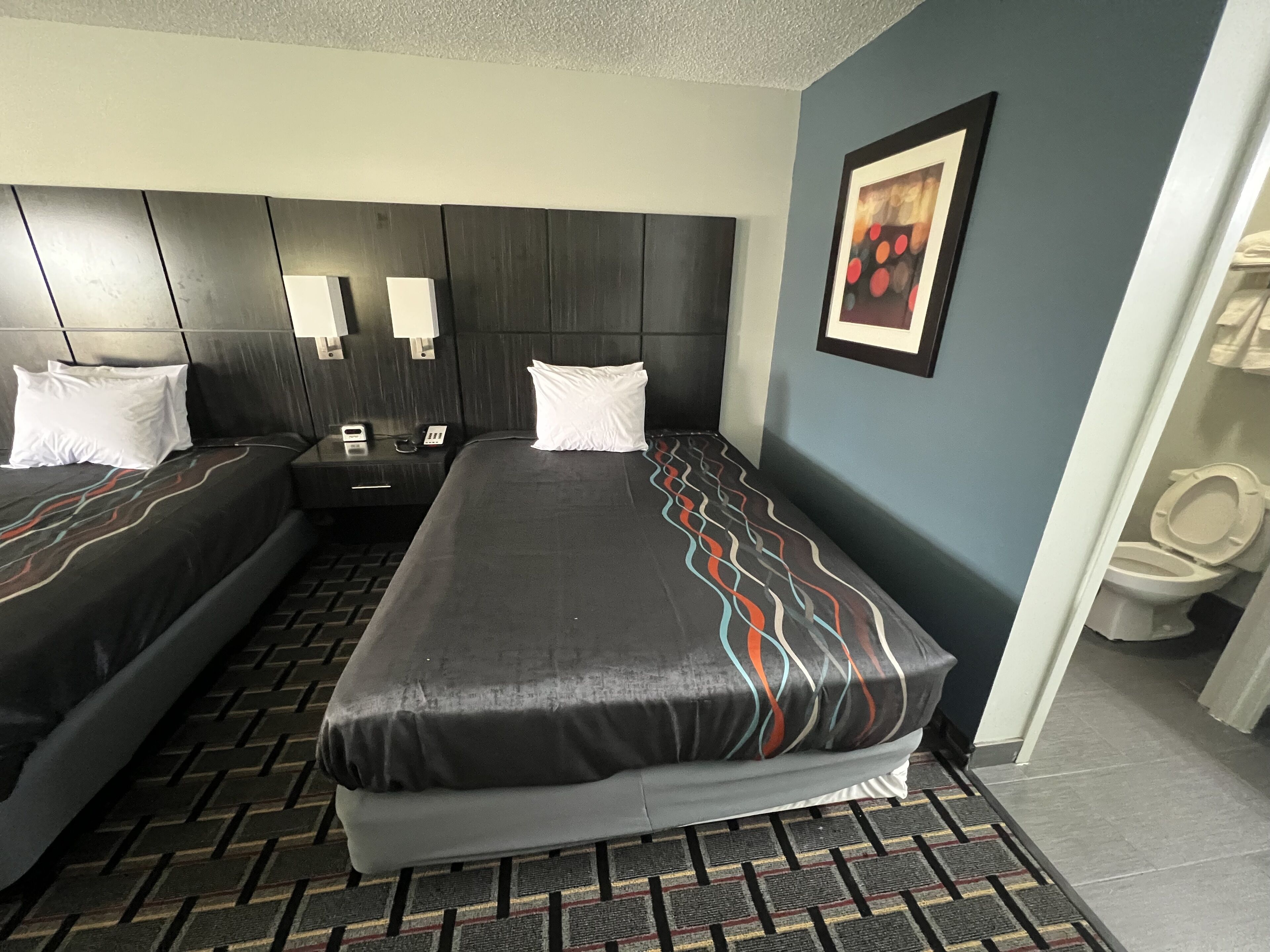 Une chambre d’hôtel avec deux lits, une tête de lit, des tables de chevet, un téléphone et un tableau encadré au mur.
