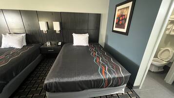 Une chambre d’hôtel avec deux lits, une tête de lit, des tables de chevet, un téléphone et un tableau encadré au mur.