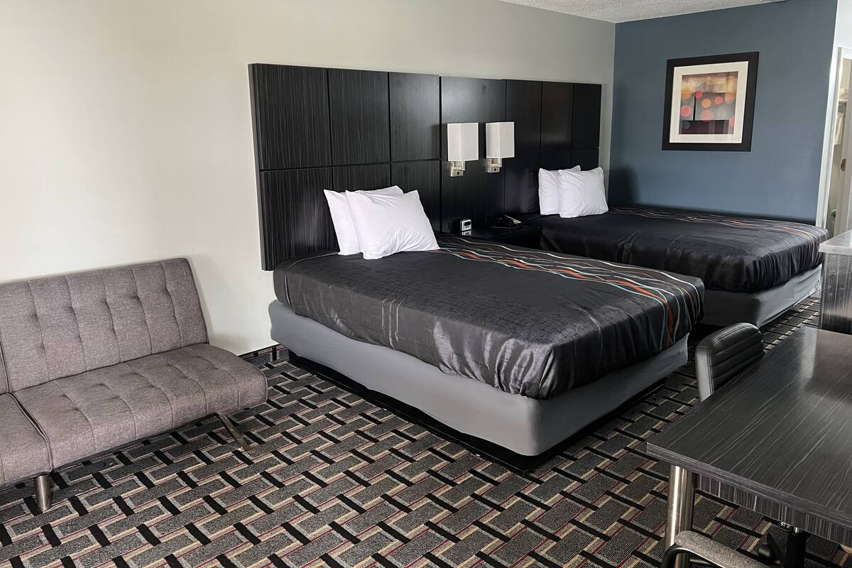 Habitación de hotel con dos camas, un sofá, una mesa y una alfombra estampada.
