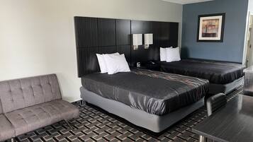 Habitación de hotel con dos camas, un sofá, una mesa y una alfombra estampada.