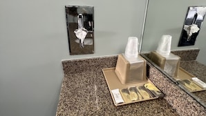 Baño con encimera de granito, espejo, secamanos y dispensador de pañuelos.
