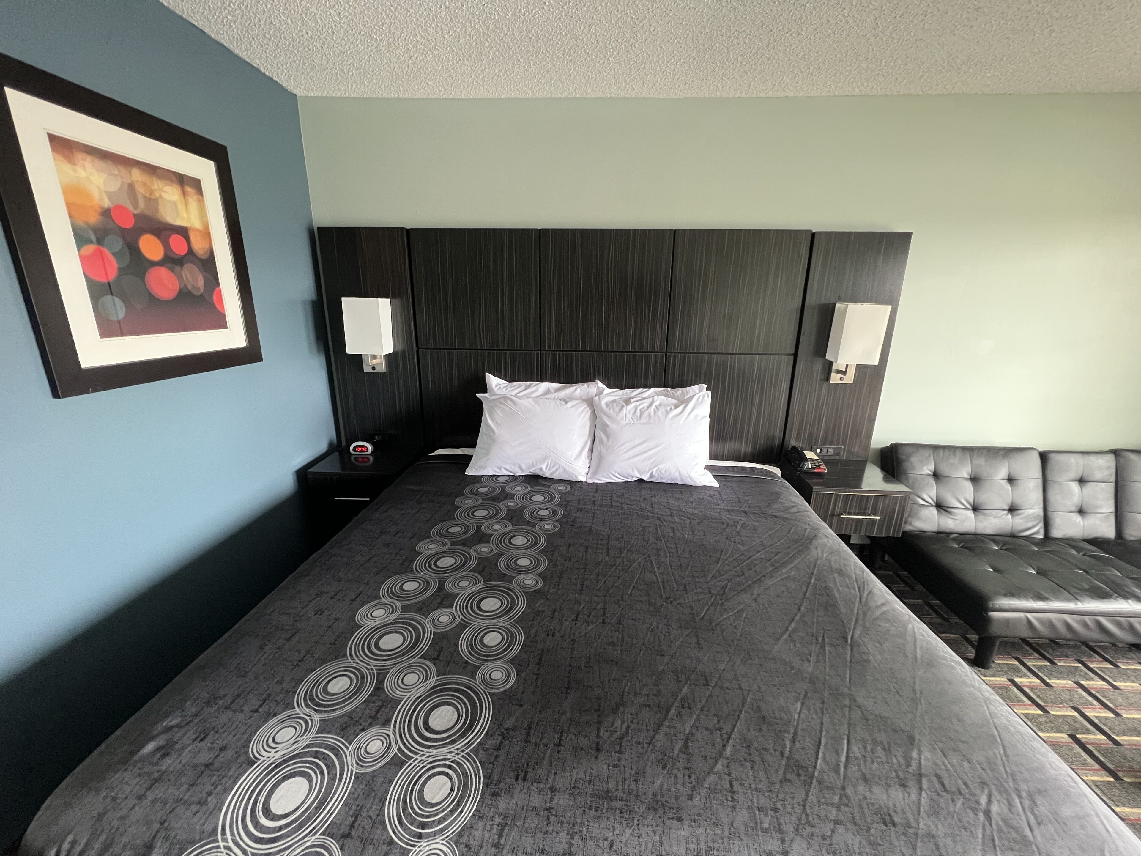 Hotelkamer met een groot bed, twee nachtkastjes, een hoofdeinde, een bank en een aan de muur hangend schilderij.