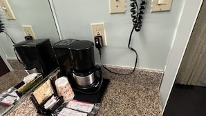 Una encimera de cocina con una cafetera, un hervidor y cápsulas de café.