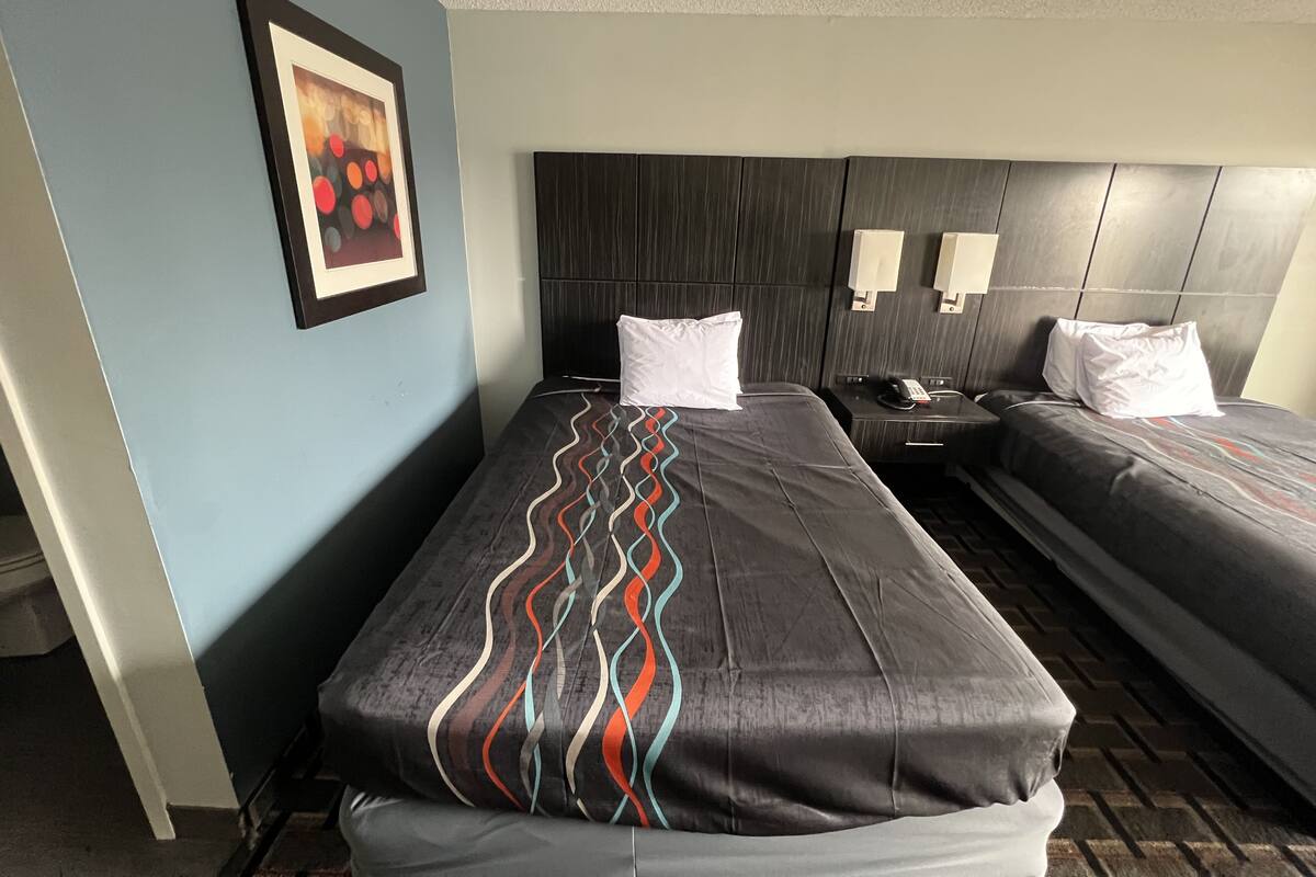 Habitación de hotel con dos camas, cabecero, lámparas de noche, teléfono y un cuadro en la pared.