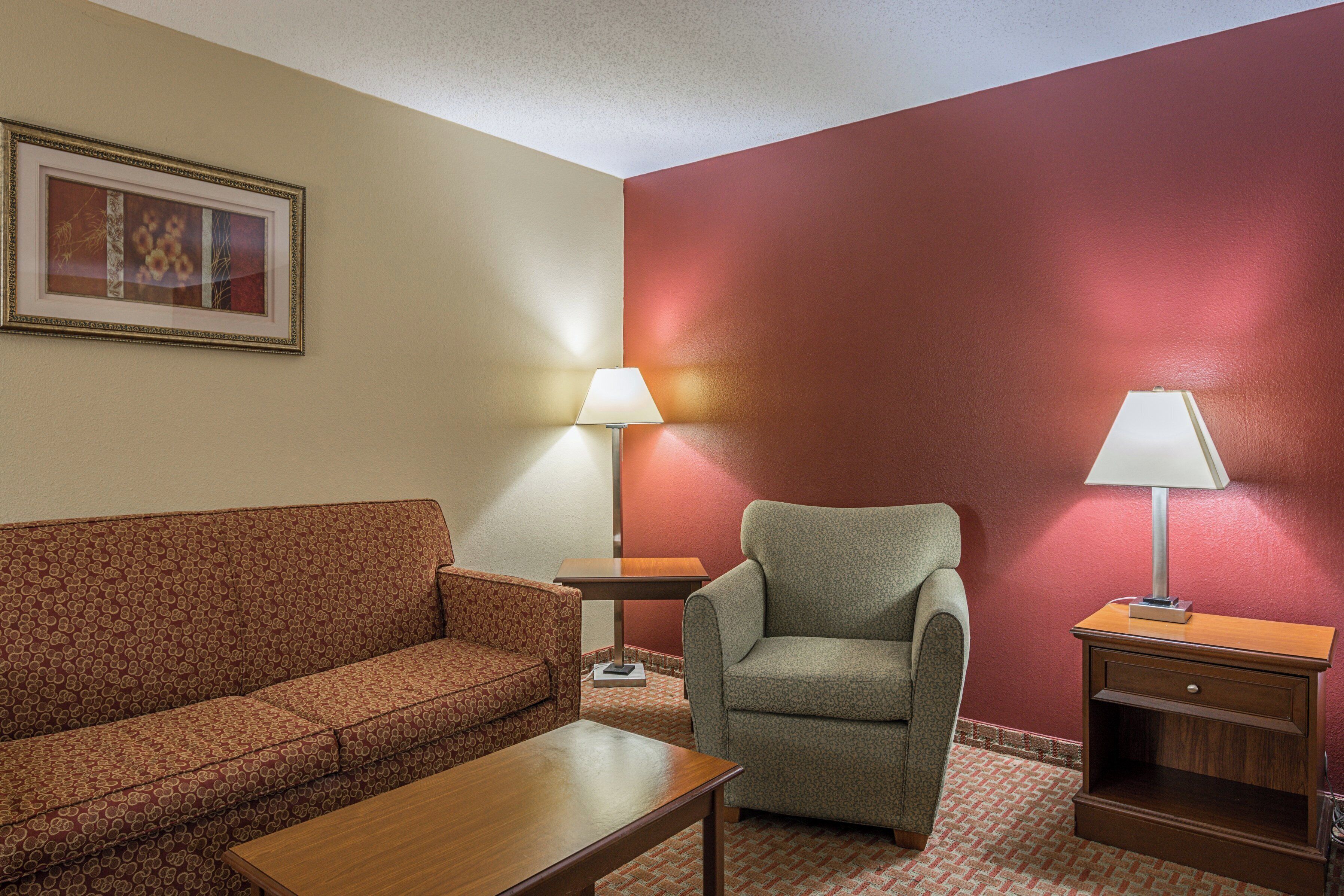 A hotel room with a sofa, armchair, table, lamps, and a framed picture on the wall.