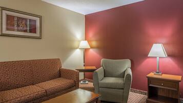 A hotel room with a sofa, armchair, table, lamps, and a framed picture on the wall.