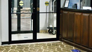 Ingresso di un hotel con porta in vetro, insegna di uscita, reception e tappeto decorato.