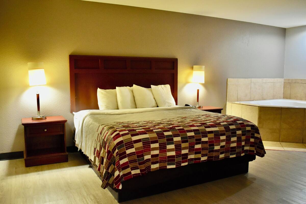 A hotel room with a large bed, two bedside lamps, a wooden headboard, and a small bedside table.