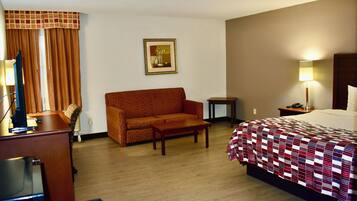 Une chambre d’hôtel comprenant un lit, un canapé, une petite table, un bureau avec un ordinateur et une lampe.