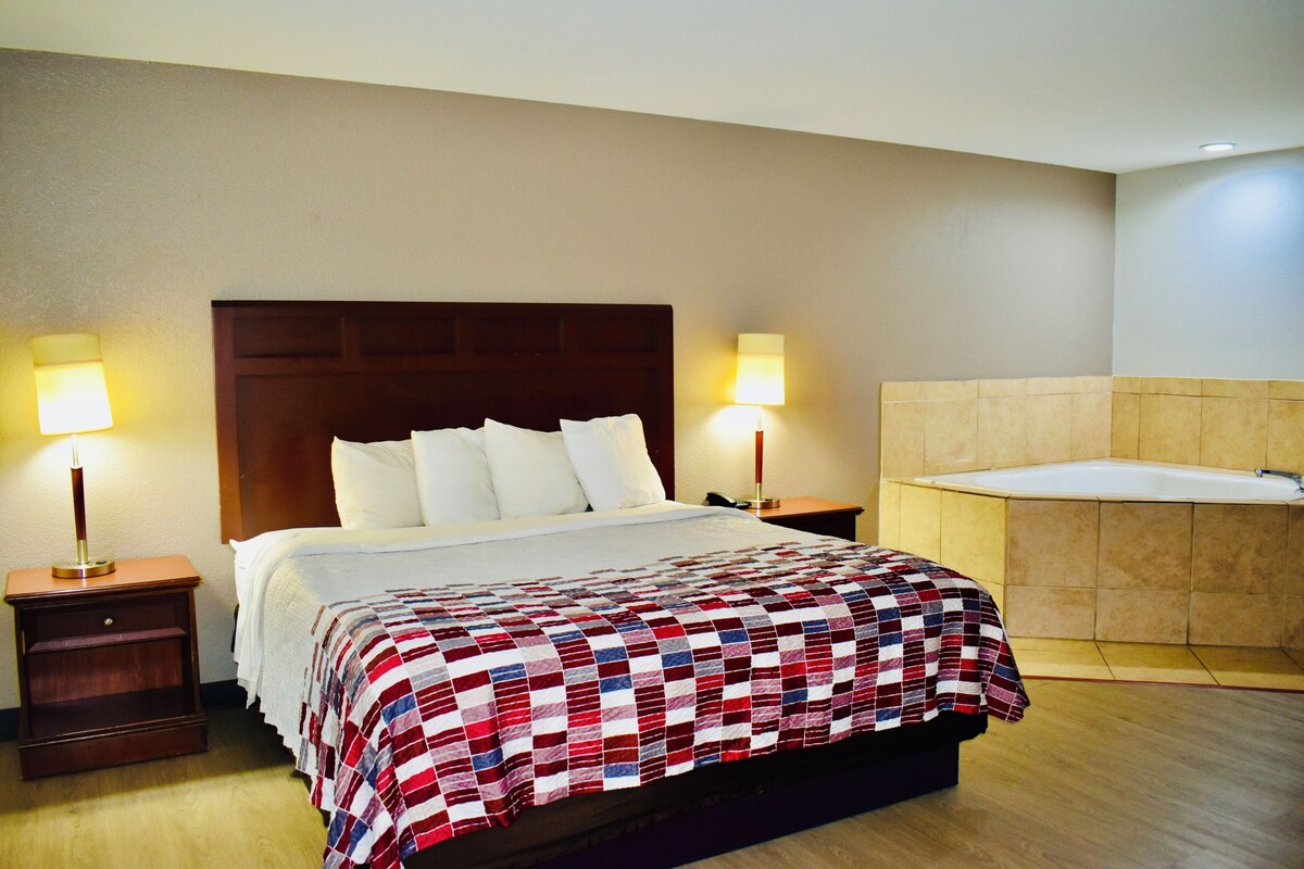 Una camera d'albergo con un letto, due abat-jour, un comodino e un bagno con una vasca.