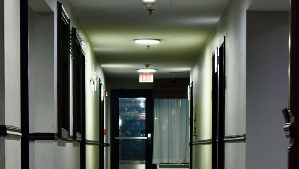 A hallway with a carpeted floor, doors on both sides, and an exit sign on the wall. - Red Roof Inn & Suites Little Rock (Little Rock)