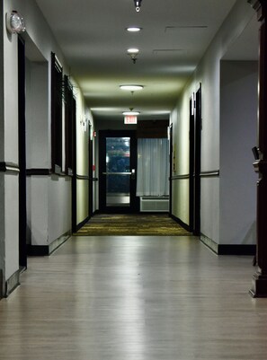 A hallway with a carpeted floor, doors on both sides, and an exit sign on the wall.