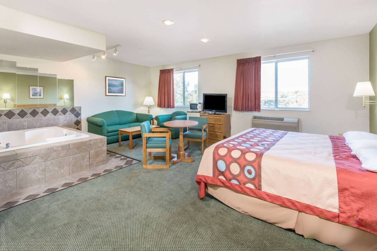 Una habitación de hotel con una cama grande, una zona de estar con una mesa y sillas, un televisor, un escritorio y una bañera.