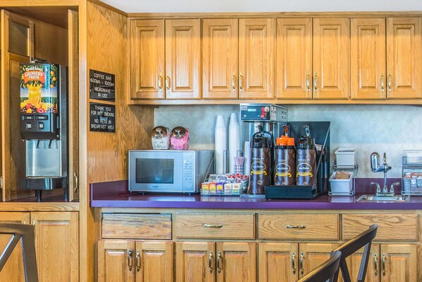 A kitchen with wooden cabinets, a coffee machine, a microwave, and a coffee bar sign. - Super 8 by Wyndham West Middlesex/Sharon Area (West Middlesex)