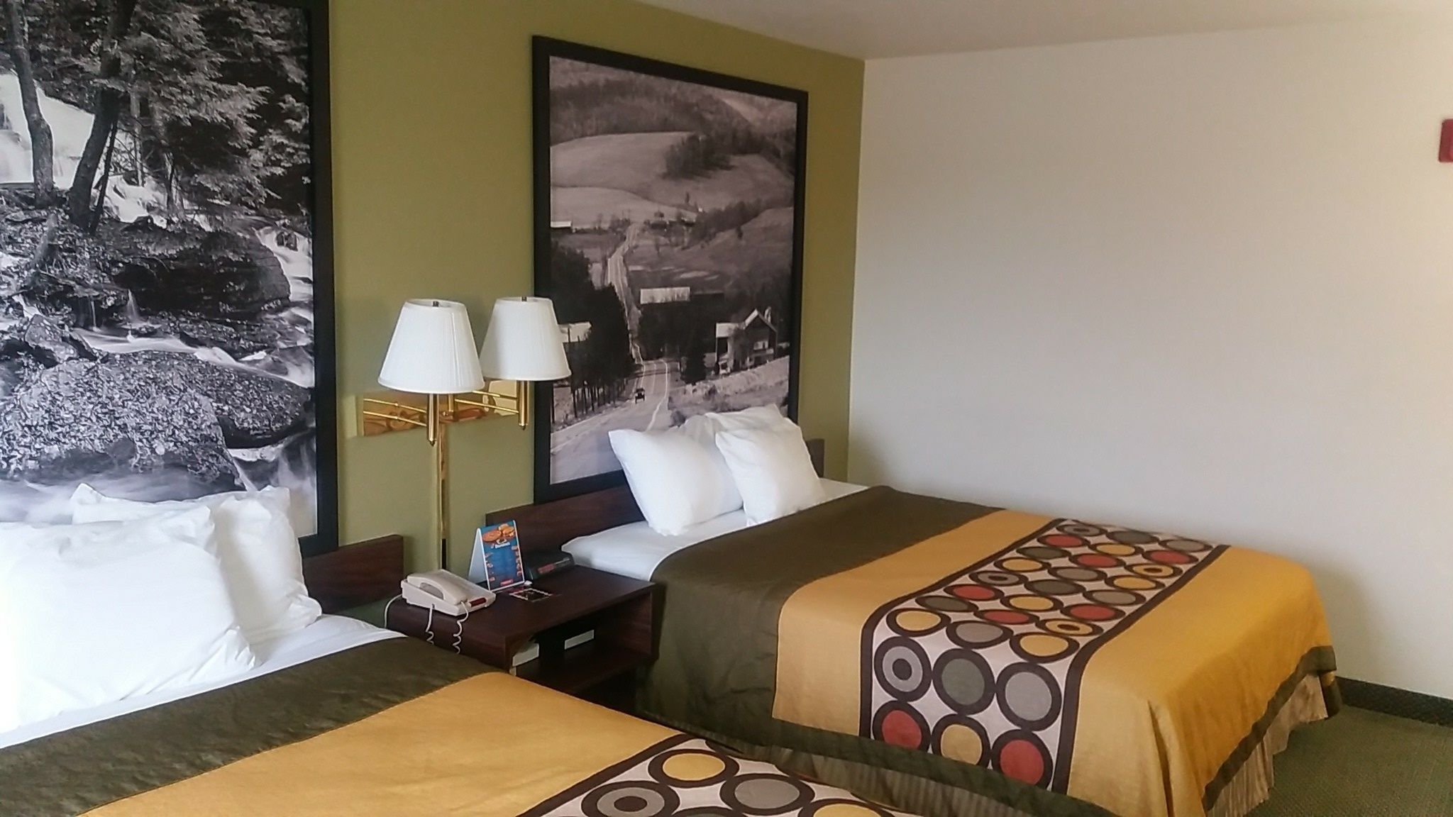 A hotel room with two beds, a nightstand, a lamp, and a large landscape painting on the wall.