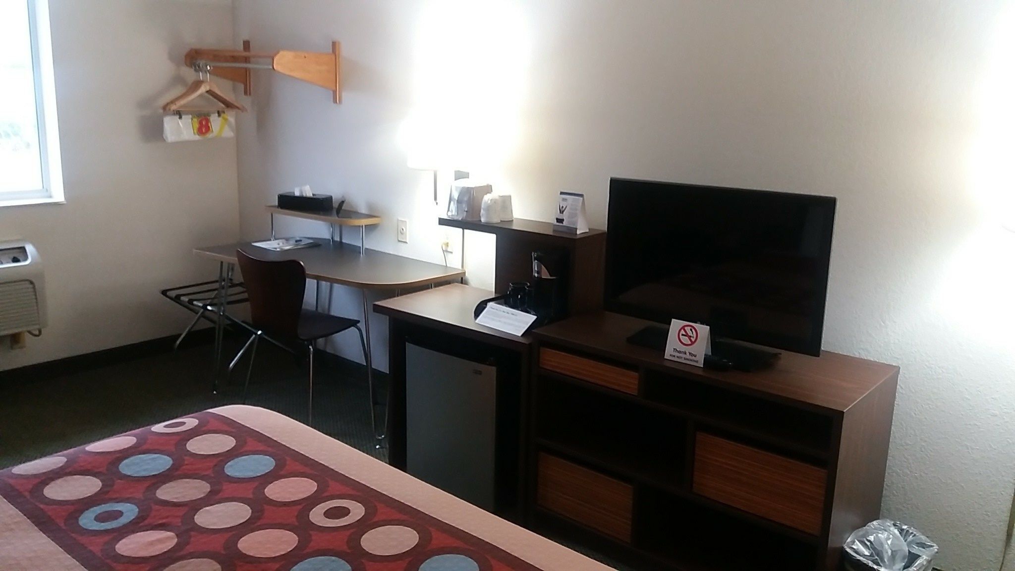 A hotel room with a bed, a desk, a chair, a TV, and a small kitchenette.