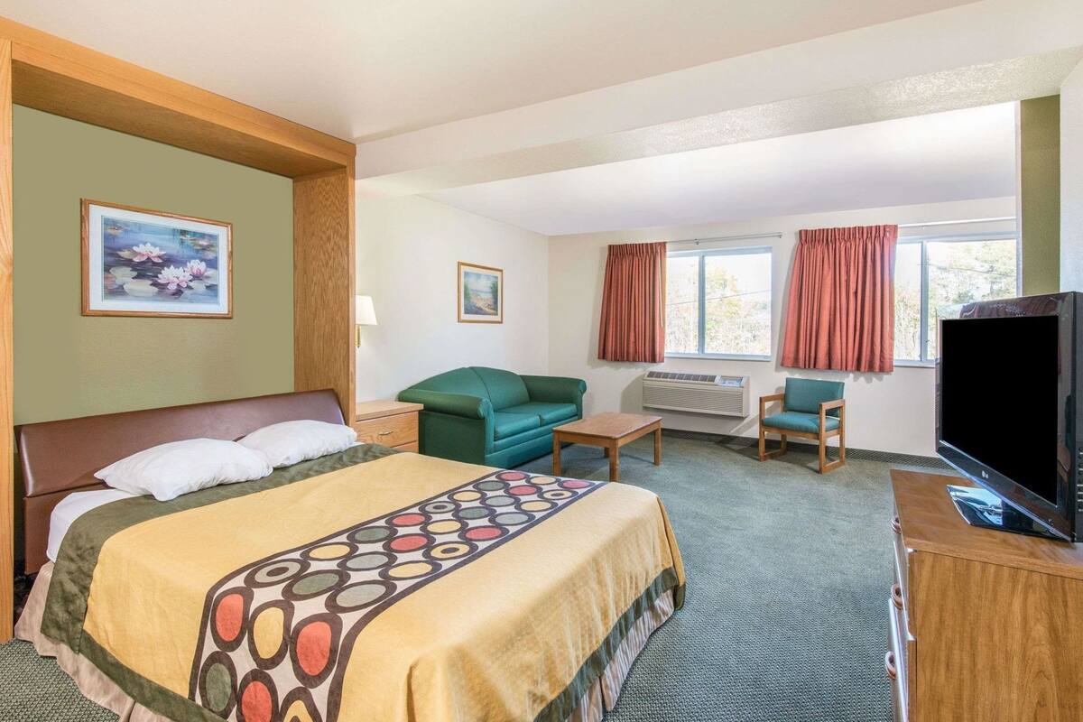 Una habitación de hotel con una cama, un sofá verde, una mesita, un televisor y una ventana con cortinas.