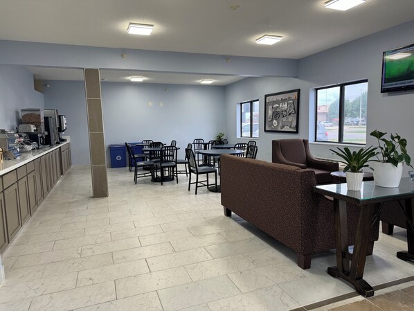 A modern office space with a dining area, a coffee station, and a comfortable seating area with a couch and chairs. - Super 8 by Wyndham Mason City (Mason City)