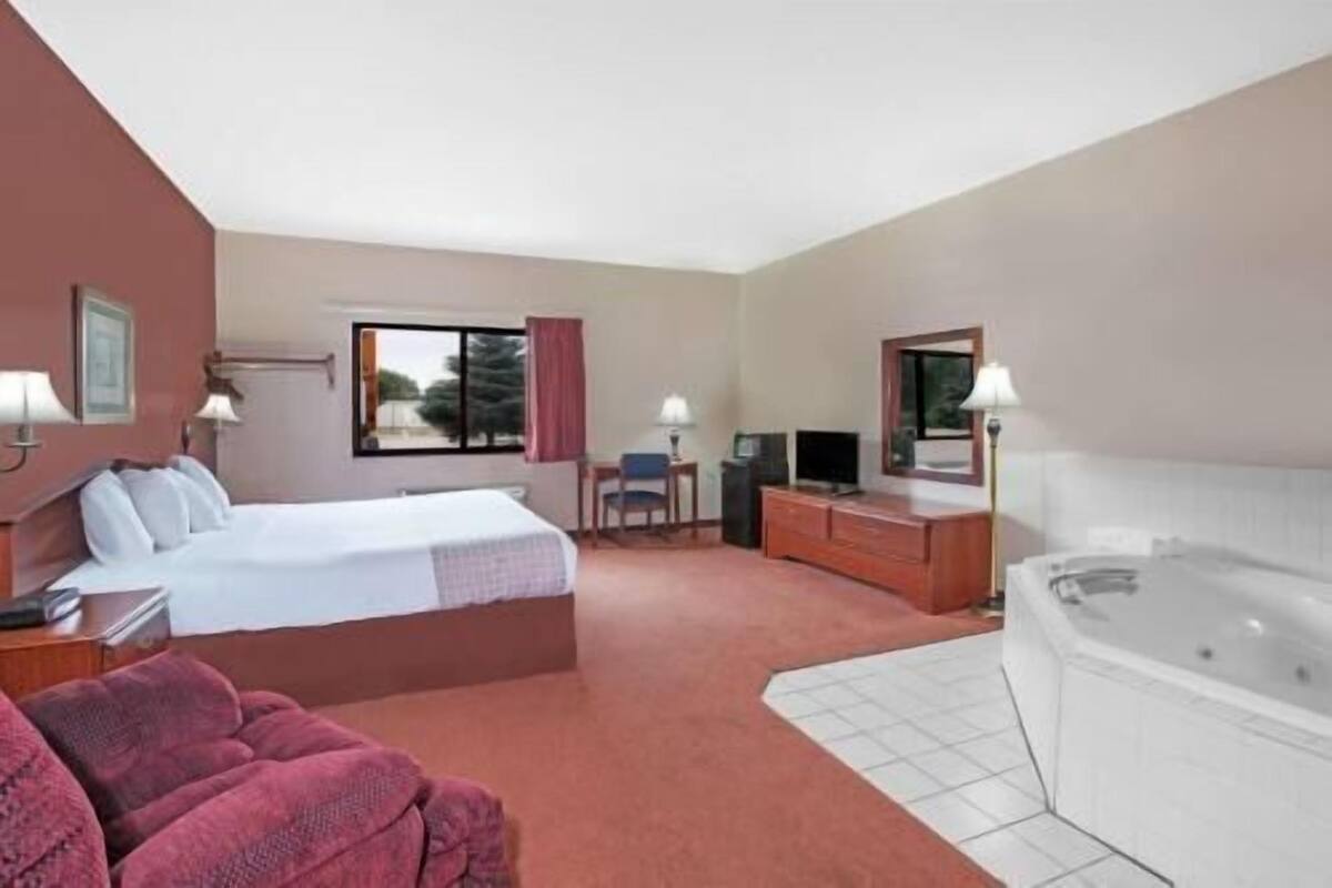 Habitación de hotel con cama, escritorio, silla, televisor y bañera de hidromasaje.