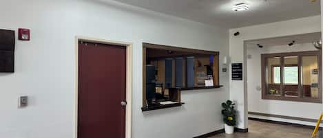 A reception area with a wooden door, a reception desk, a bulletin board, and a fire alarm.
