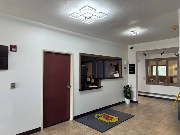 Un área de recepción con una puerta de madera, un mostrador, un tablón de anuncios y un detector de incendios.