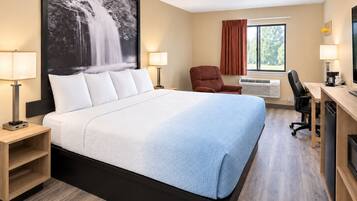 A hotel room with a large bed, a desk with a computer, a chair, a TV, and a window with curtains.