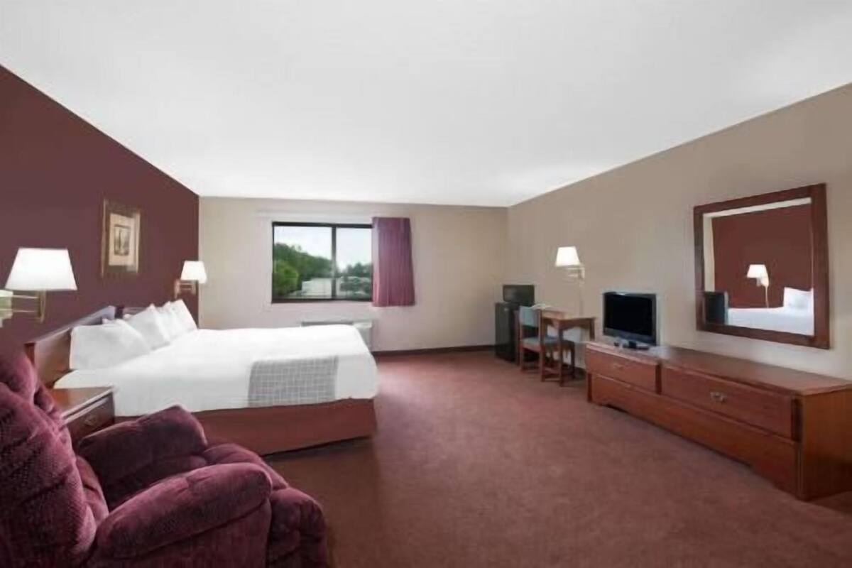 Habitación de hotel con una cama, un escritorio con computadora, un televisor y un espejo grande.