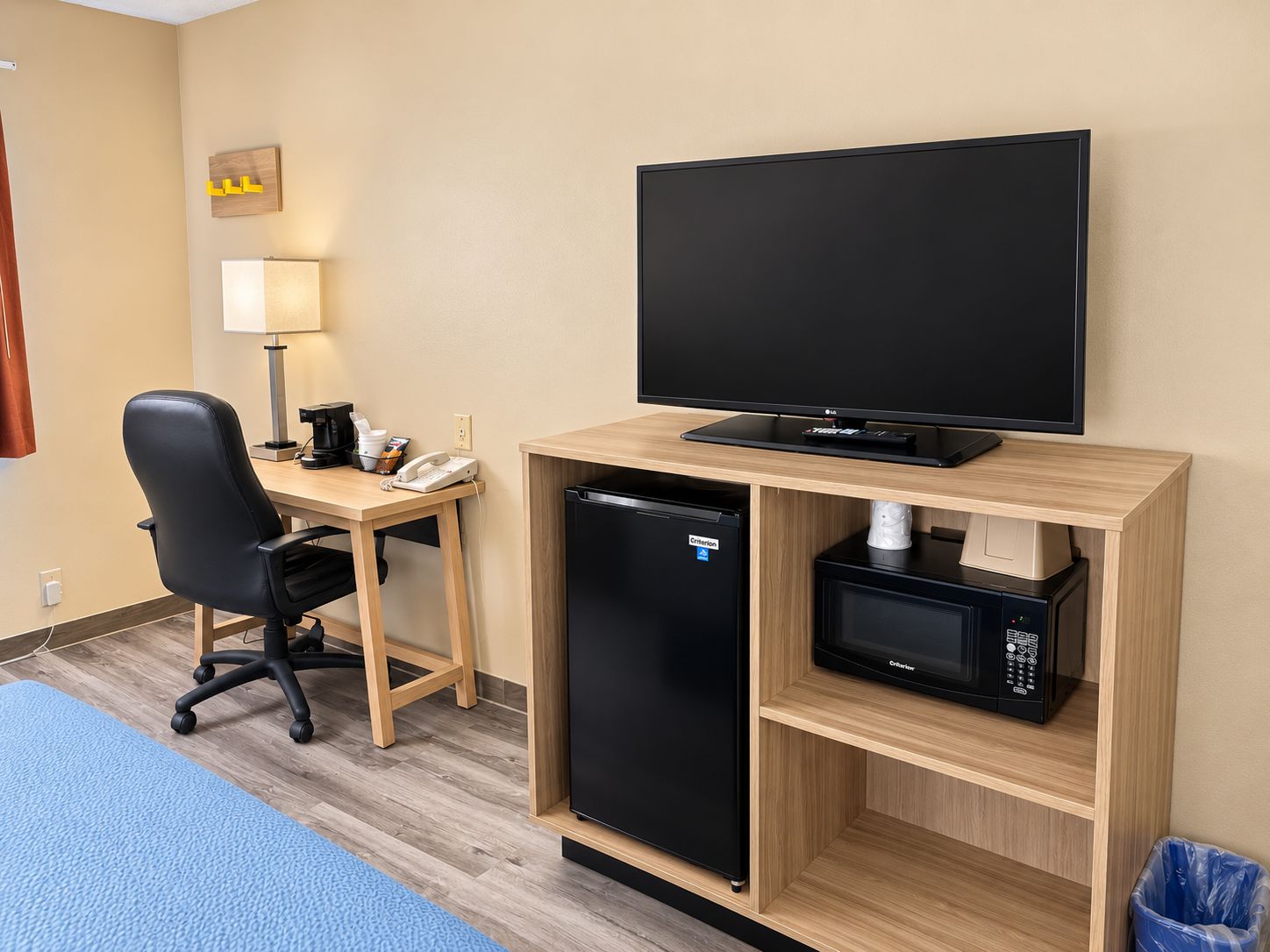A hotel room with a desk, chair, television, refrigerator, microwave, and trash bin.