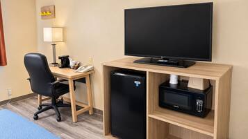 A hotel room with a desk, chair, television, refrigerator, microwave, and trash bin.