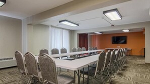 Ein Konferenzraum mit einem langen Tisch, Stühlen, einem Fernseher und einem Fenster mit Vorhängen.