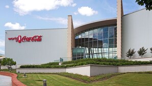 Ein modernes Gebäude mit Coca-Cola Logo, großen Glasfenstern und einer geschwungenen Fassade.