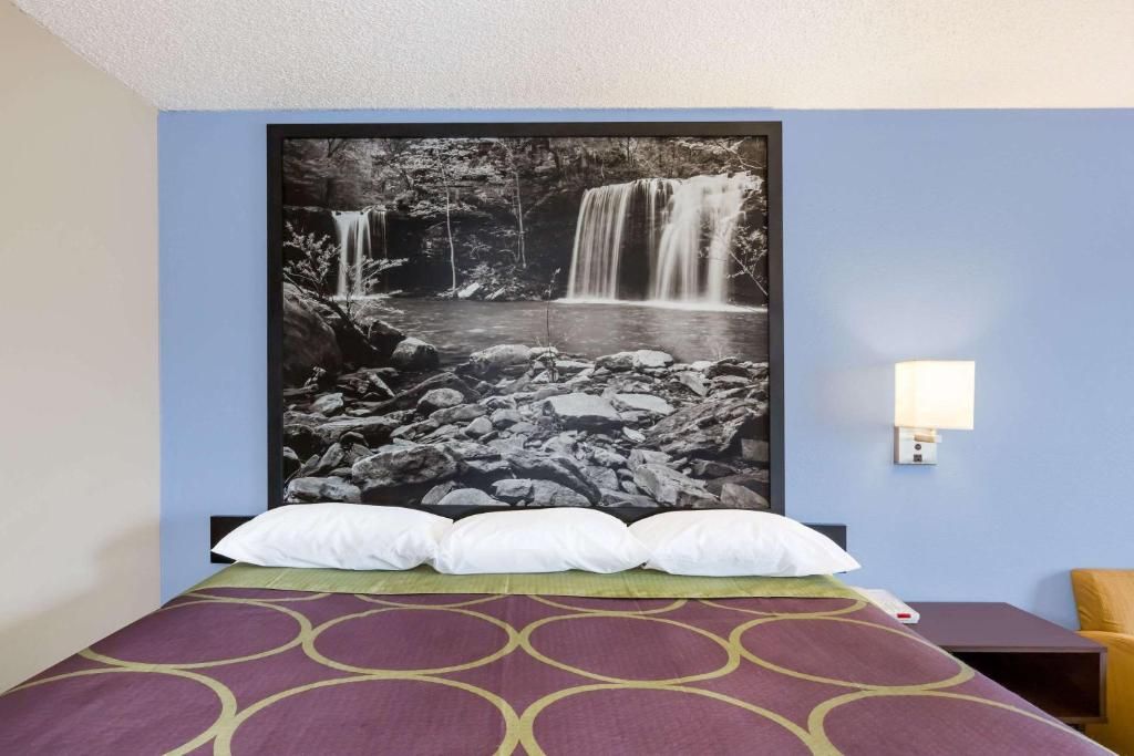 Une chambre d’hôtel avec un lit, une lampe fixée au mur et un grand tableau représentant une cascade.
