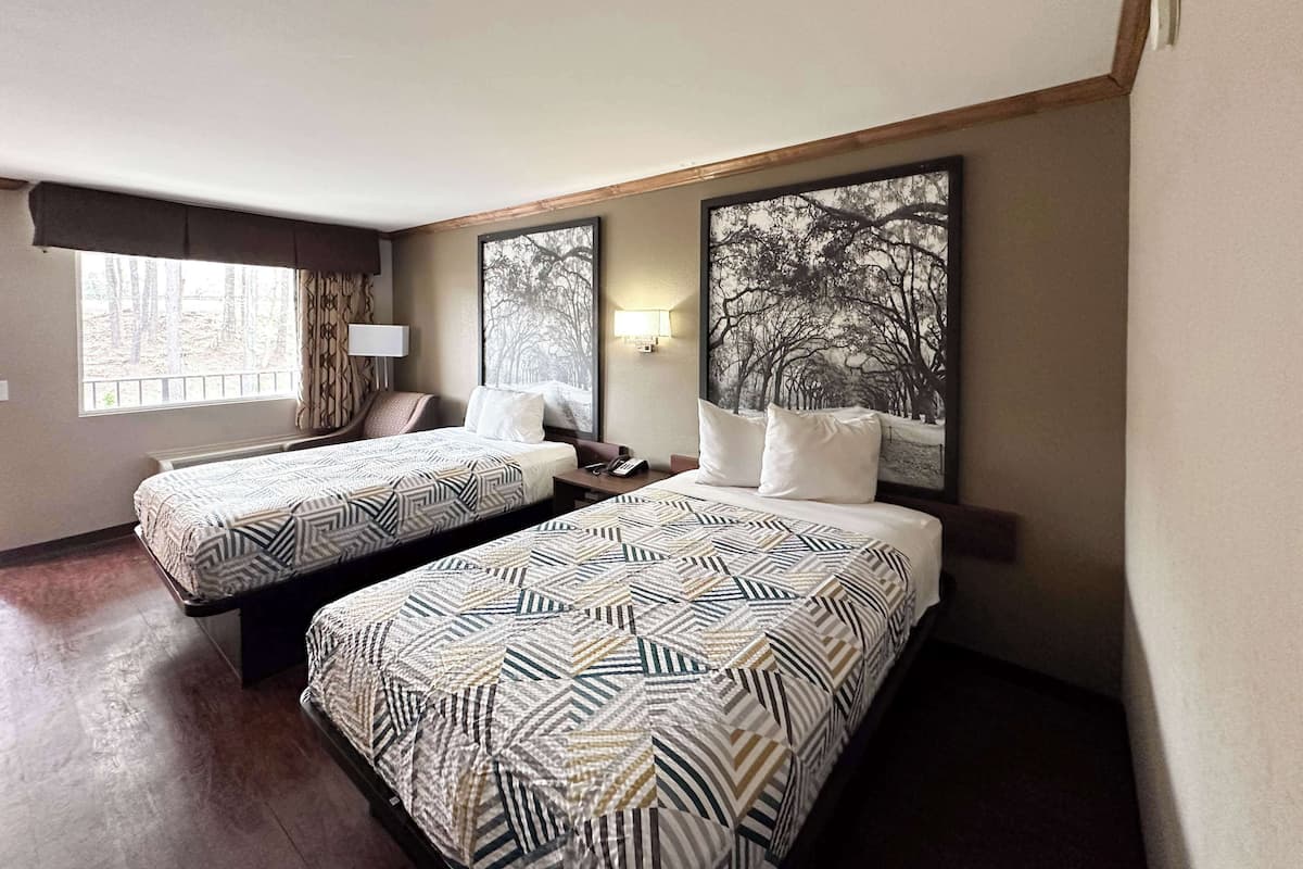 Une chambre d’hôtel avec deux lits, chacun agrémenté de draps à motifs, une grande fenêtre donnant sur des arbres et un tableau représentant une forêt accroché au mur.