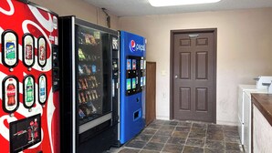 Ein Automatenbereich mit Coca-Cola- und Pepsi-Automaten, einem Kühlschrank und einer Tür mit der Aufschrift 'Nur für Mitarbeiter'.
