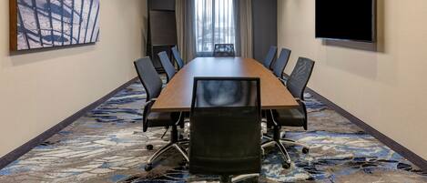 A conference room with a long table, chairs, a large abstract painting, a TV, and a view through the window.