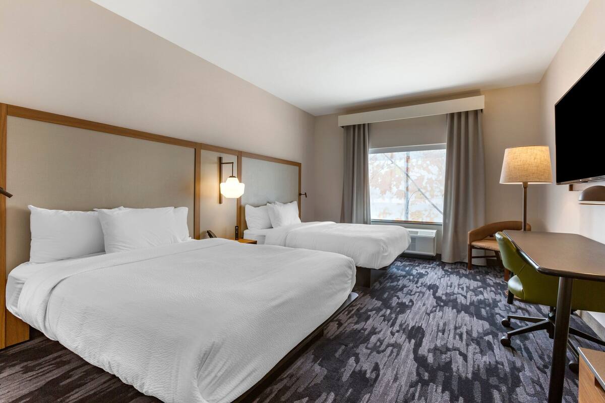 A hotel room with two beds, a desk, a chair, a TV, and a window with curtains.