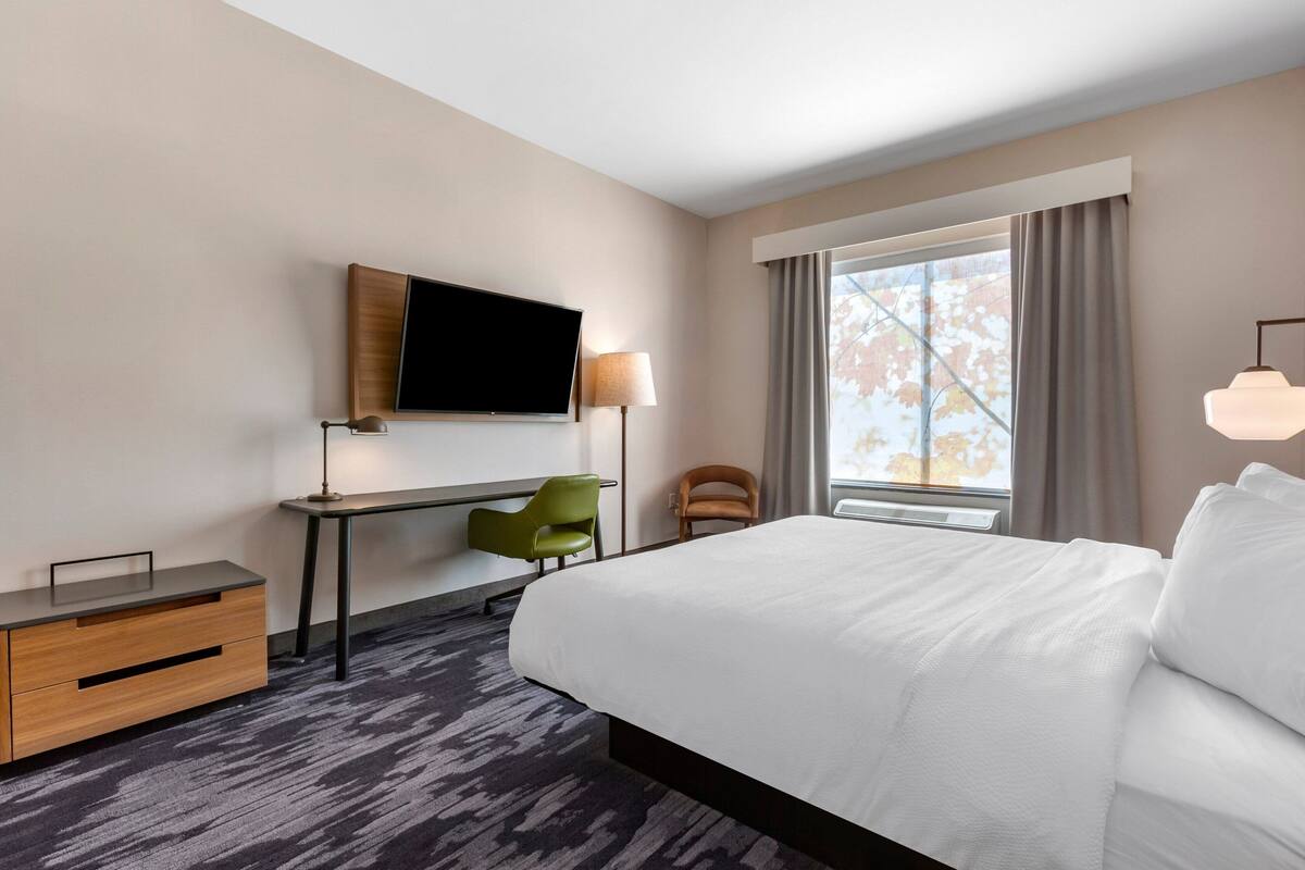 A hotel room with a large bed, a desk with a chair, a television, and a window with curtains.