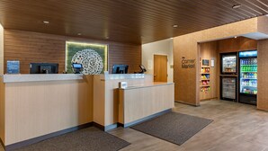A reception area with a wooden reception desk, a digital kiosk, and a refrigerator stocked with beverages. - Fairfield by Marriott Inn & Suites Sandusky (Sandusky)